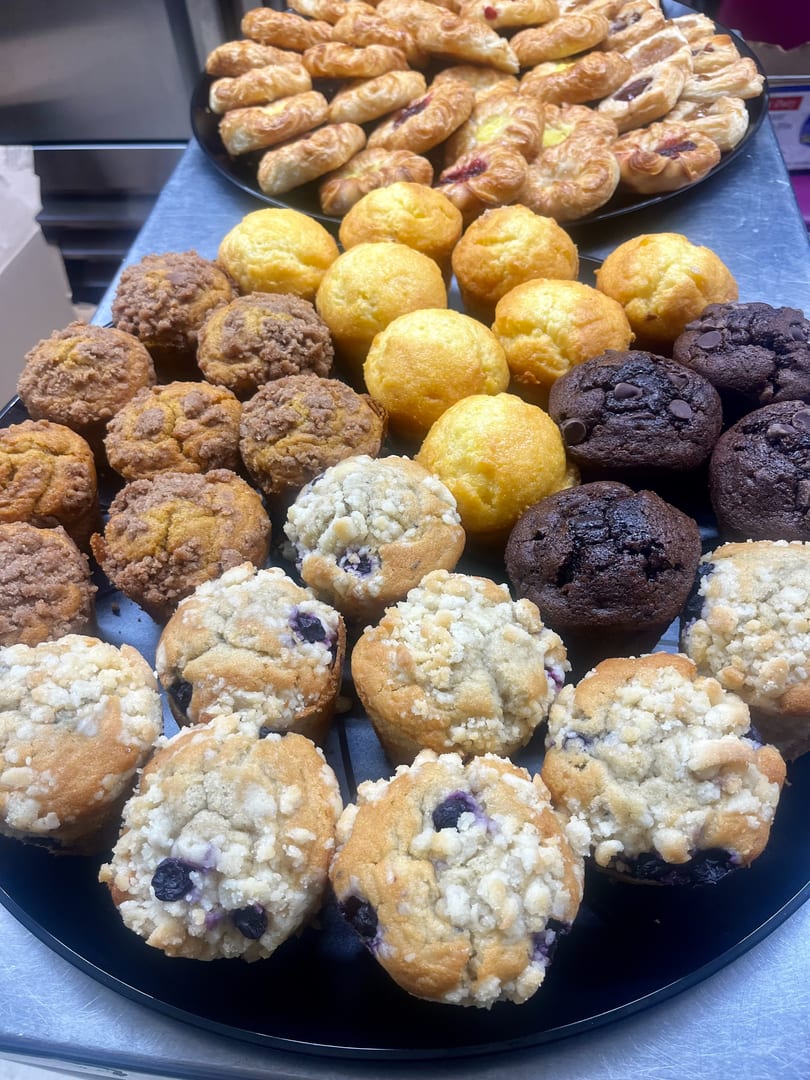 A black tray filled with assorted muffins, including blueberry, chocolate chip, and streusel-topped varieties.