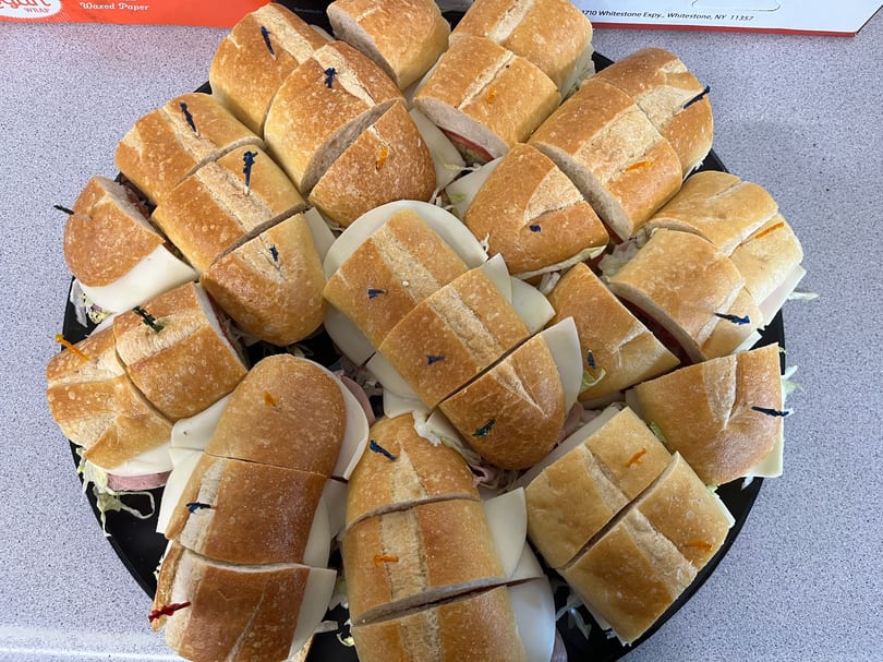 A platter of sliced submarine sandwiches with various fillings, garnished with colorful toothpicks.