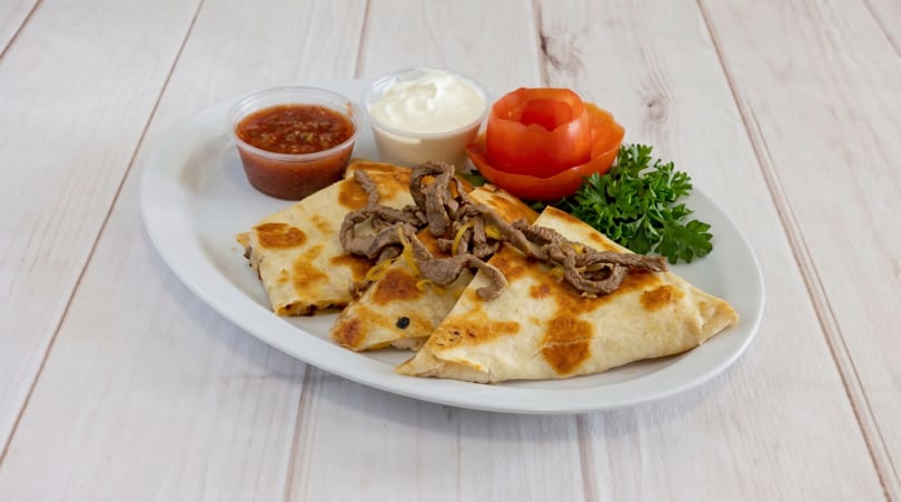 Steak quesadillas with salsa, sour cream, a tomato rose, and parsley on a white plate.