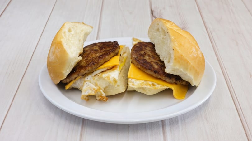 Two halves of a breakfast sandwich with sausage, egg, and cheese on a white plate.
